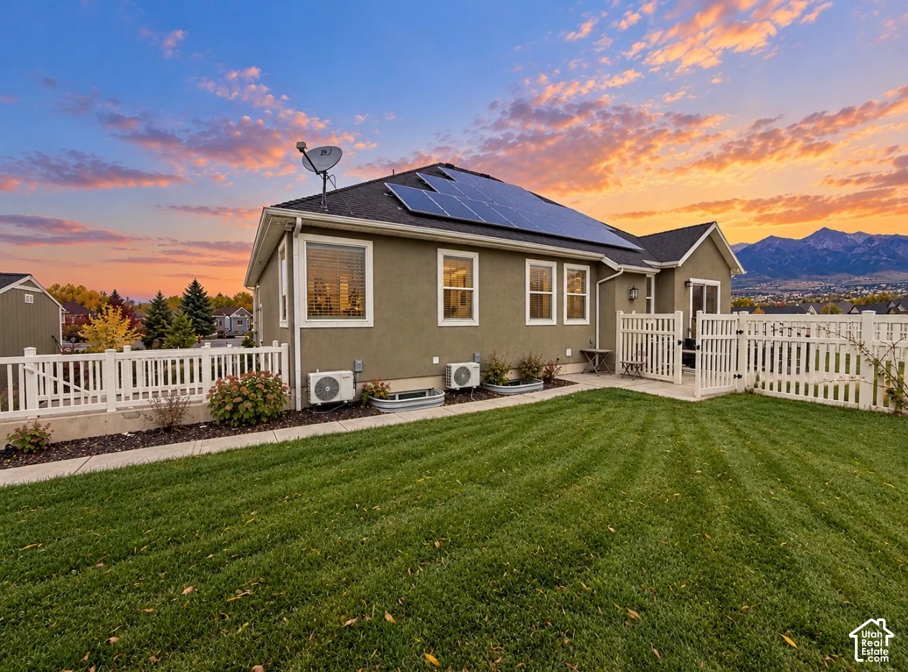 Exterior elevation featuring a stucco finish, rooftop solar panel array, fenced backyard, and mountain backdrop