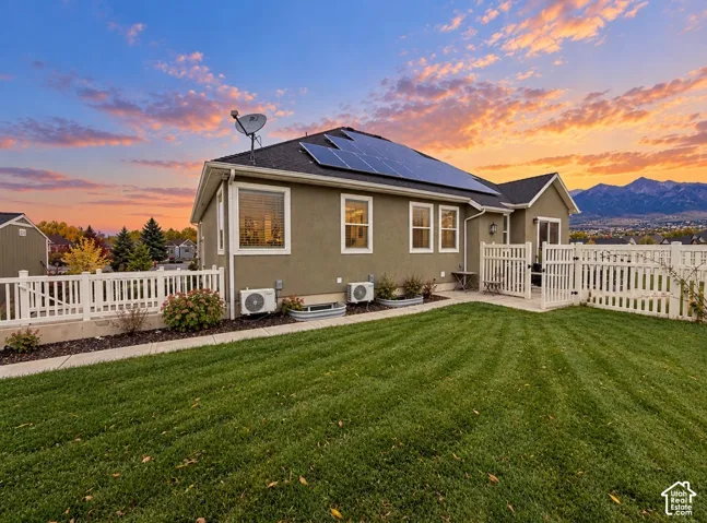 Exterior elevation featuring a stucco finish, rooftop solar panel array, fenced backyard, and mountain backdrop