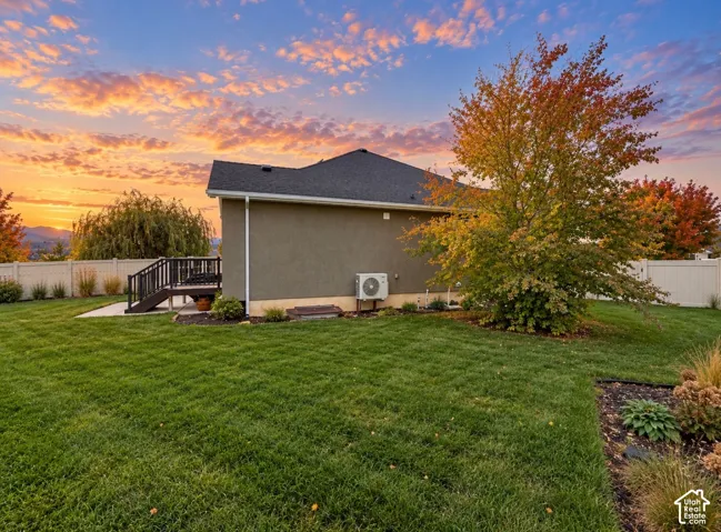 Expansive backyard featuring a manicured lawn, raised wooden deck, white privacy fencing, and mature landscaping