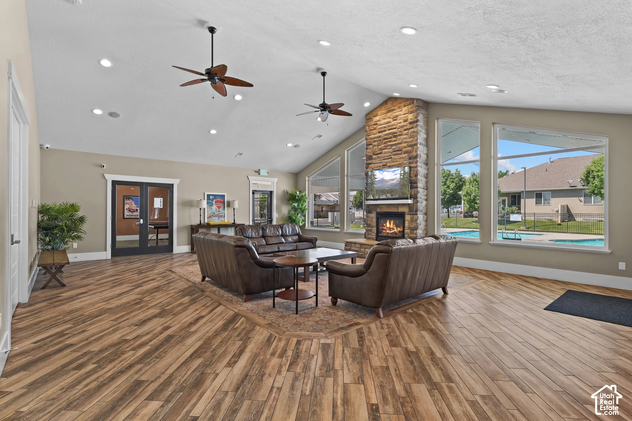 Vaulted ceiling, stone-surround fireplace, wood-finish flooring, dual ceiling fans, and expansive windows