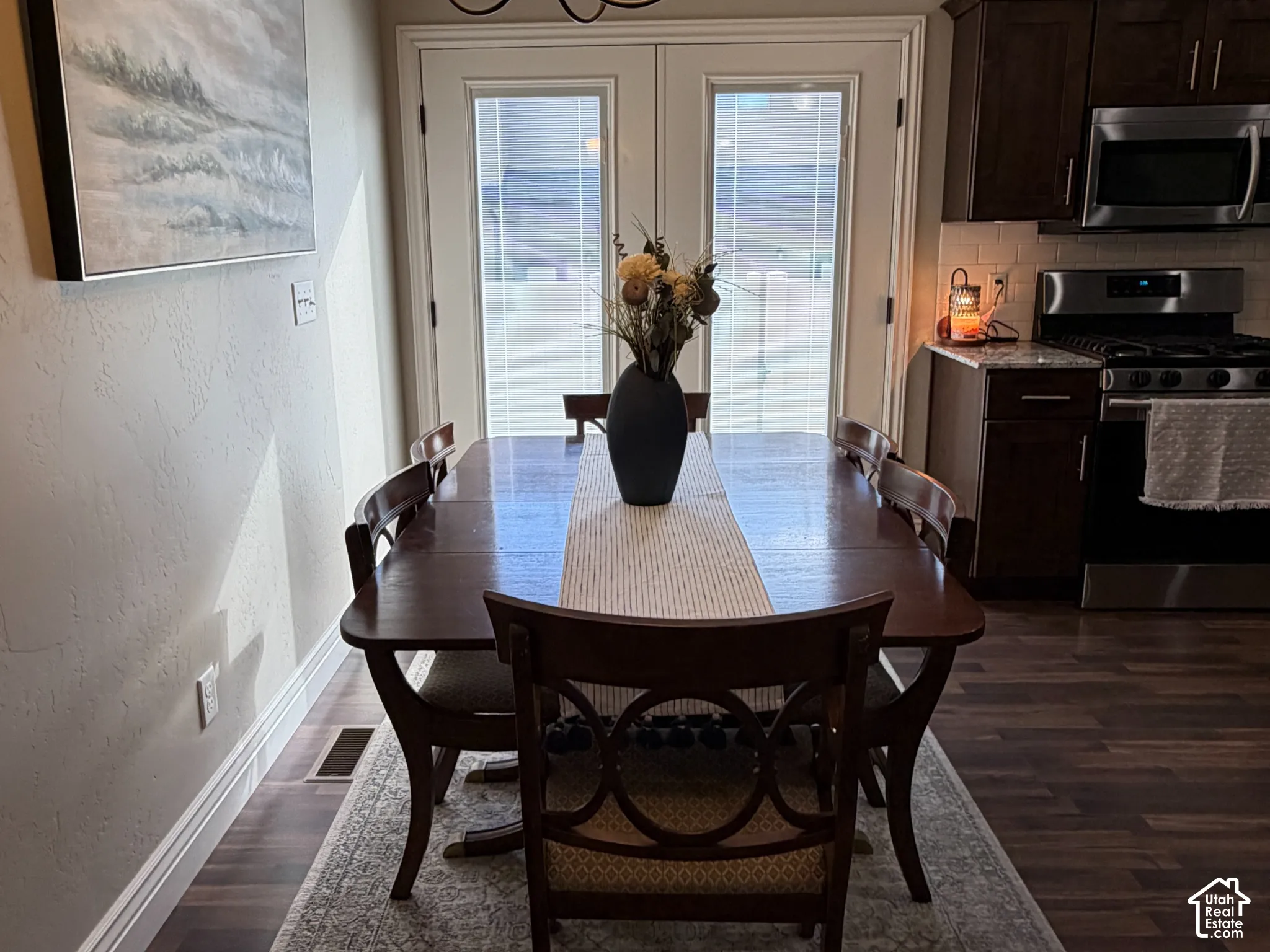 Dining space featuring wood-finish flooring, dark-toned cabinetry, stainless steel appliances, a classic multi-arm chandelier, and glass-paneled double doors