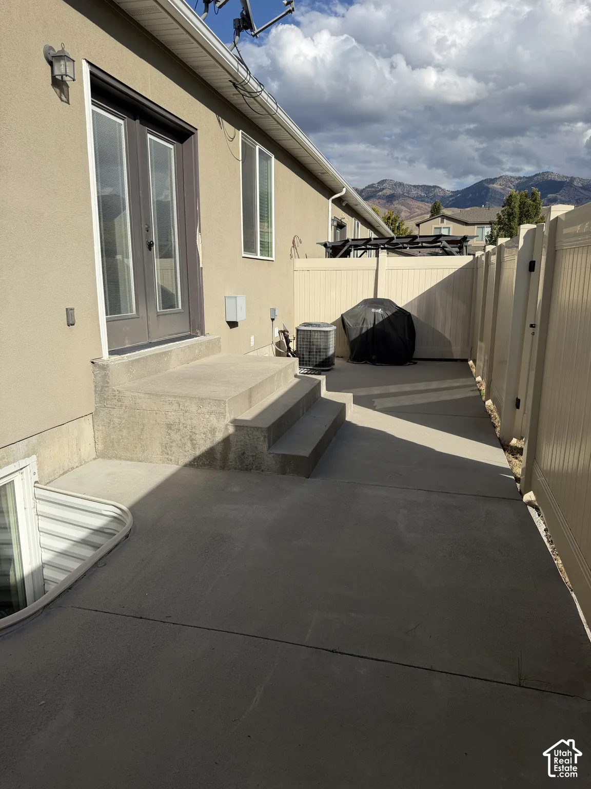 Concrete patio featuring double glass doors, a concrete staircase, mountain backdrop, and enclosed vinyl fencing