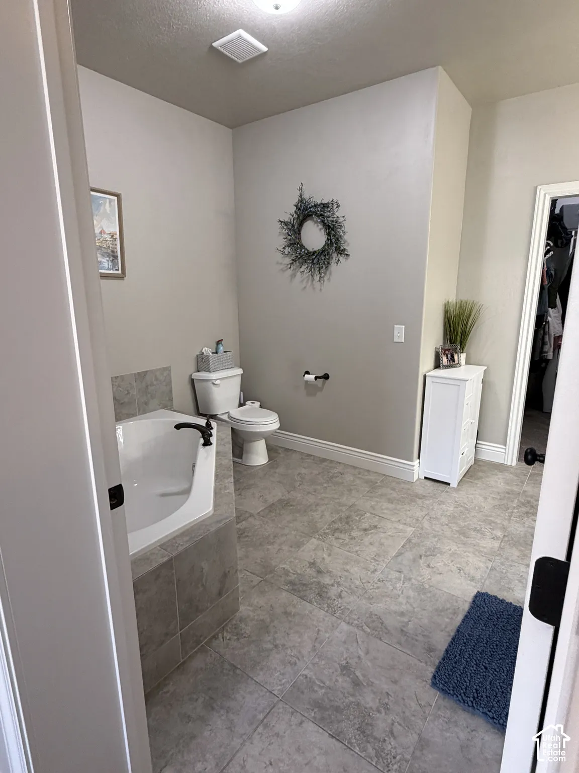 Primary suite bathroom offers a corner soaking tub with tile surround, matte black faucet, and stone-finish floor tile