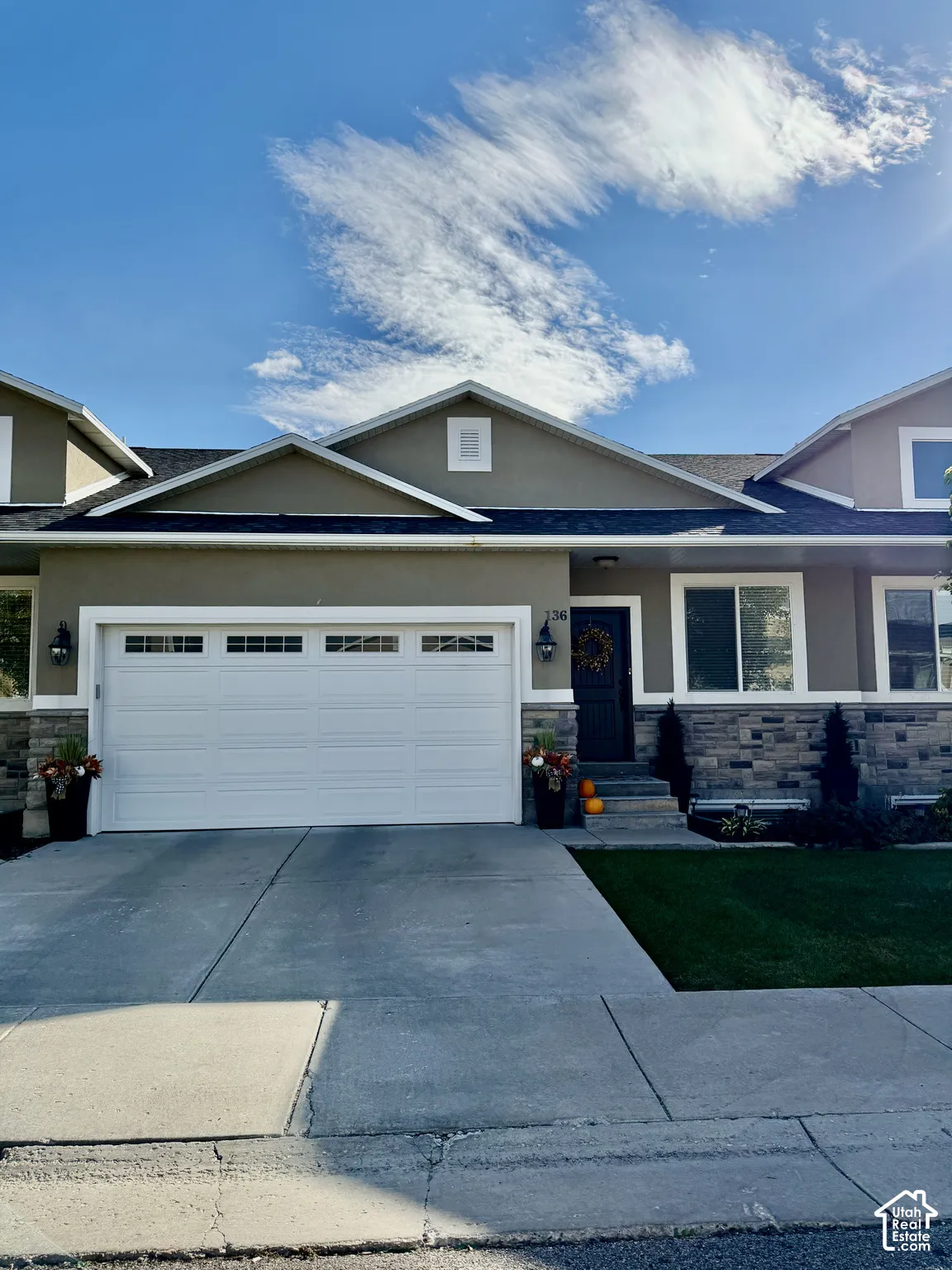Multi-level exterior featuring a two-car garage, stone veneer siding, dual gabled rooflines, and a concrete driveway