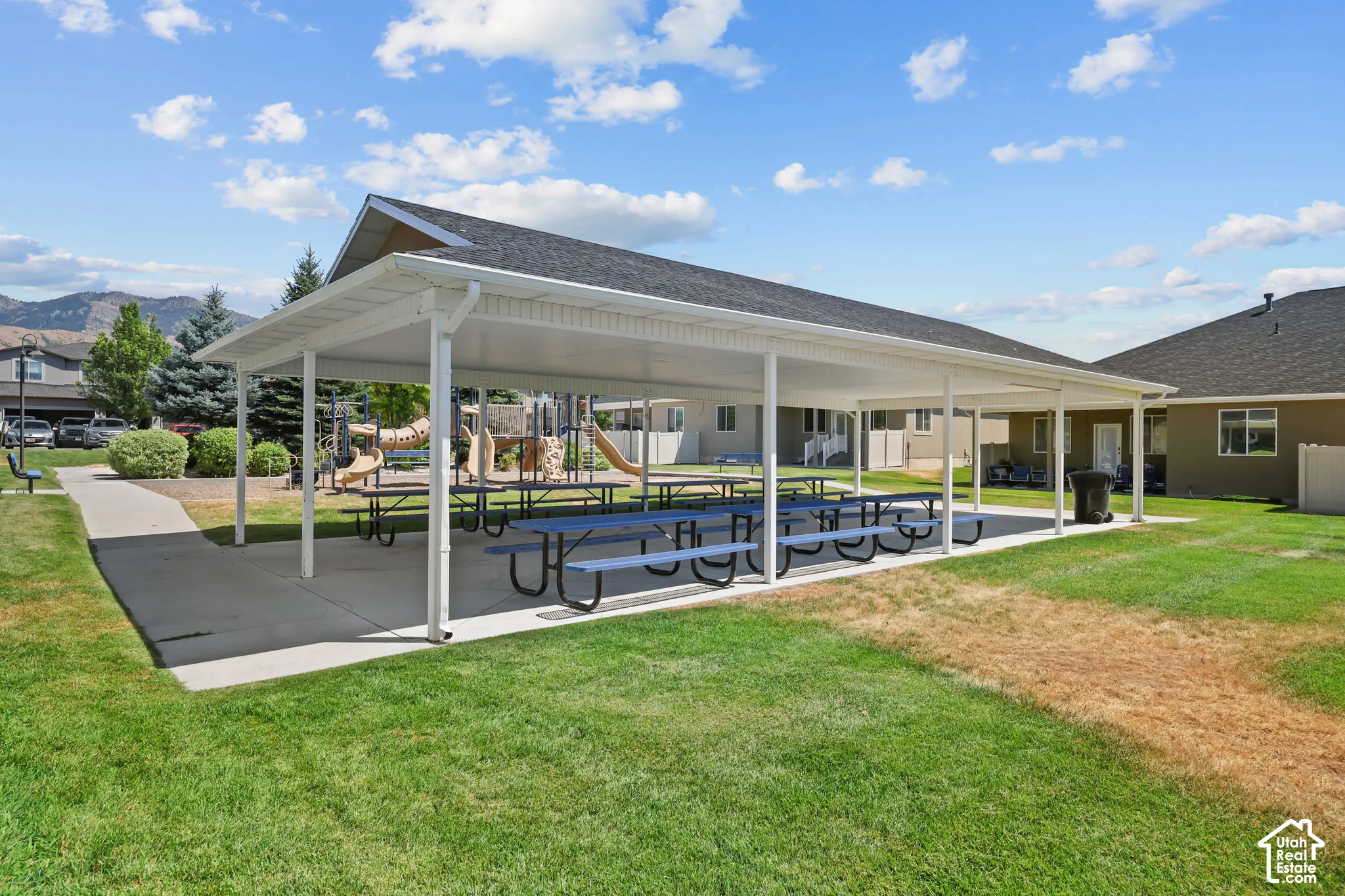Covered outdoor pavilion with a concrete foundation, metal roofing, support columns, and mountain backdrop