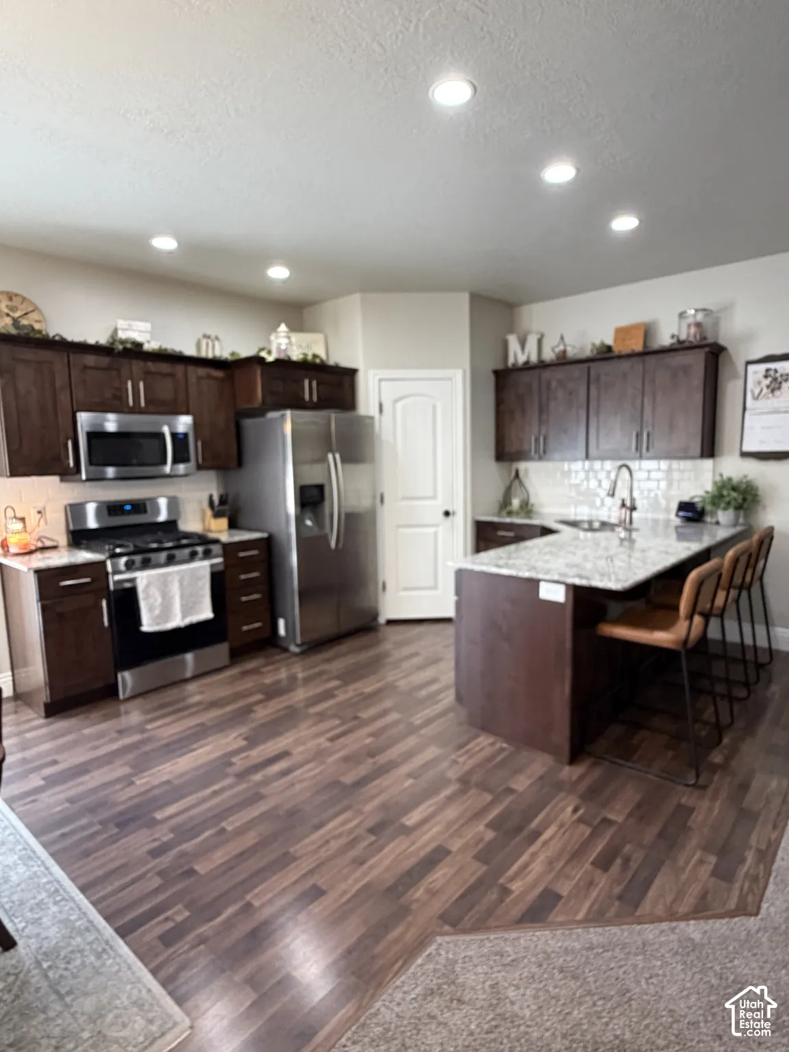 Kitchen featuring dark wood-finish cabinetry, stone-surface countertops, stainless steel appliances, a peninsula with seating, and recessed lighting