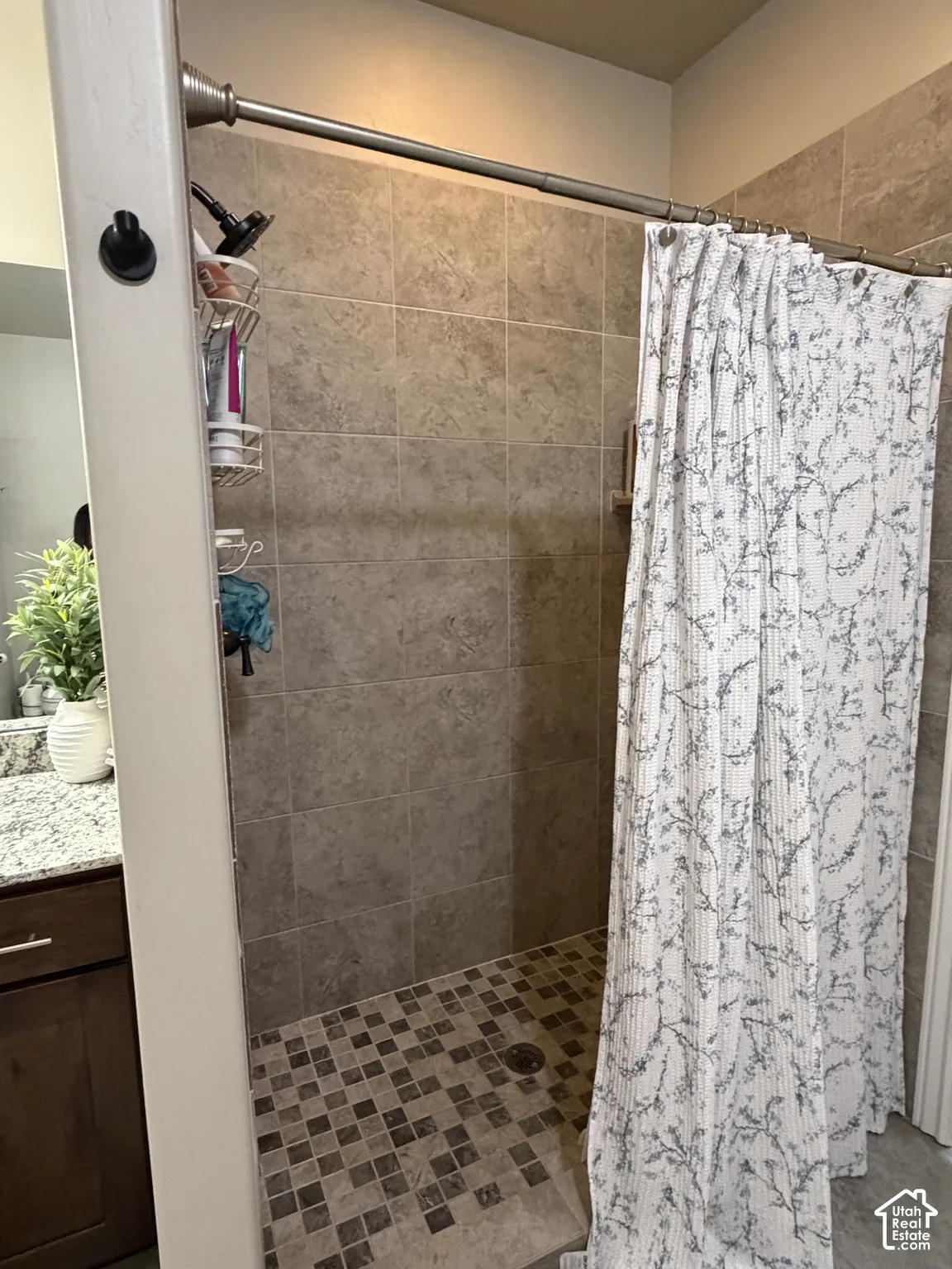 Walk-in shower featuring floor-to-ceiling neutral tile surround, multi-tone mosaic tile flooring, and a fixed shower head