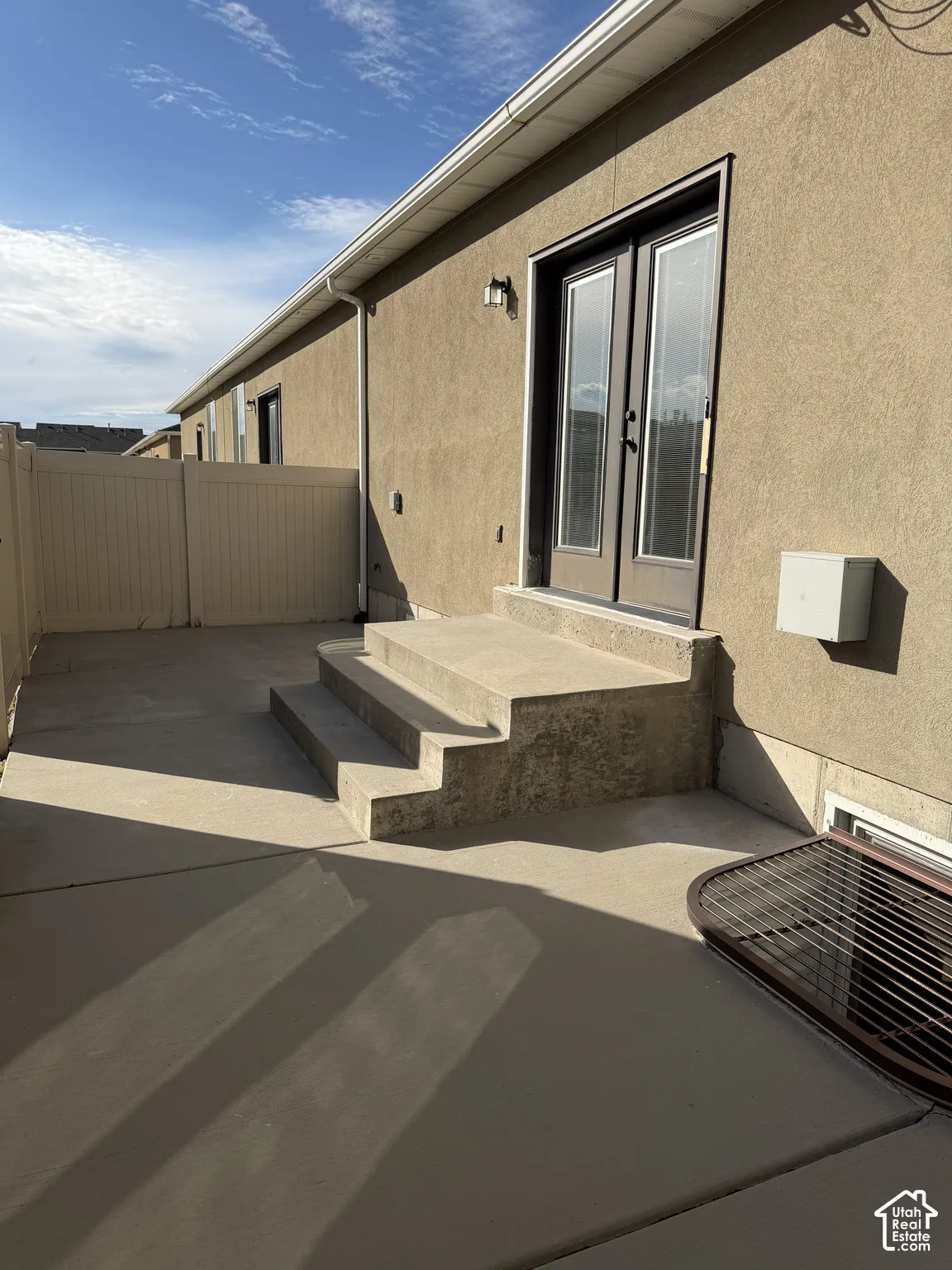 Stucco exterior with French-style double doors, concrete patio, concrete steps, and vinyl privacy fencing