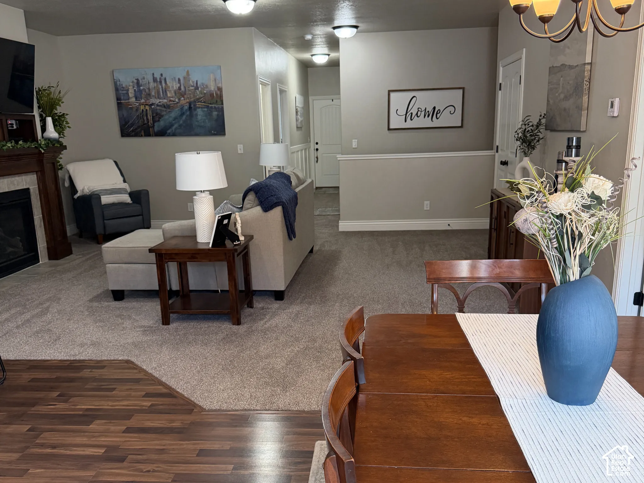 Wood-finish flooring, fireplace with a mantle, flush-mount ceiling lighting, and a multi-arm hanging chandelier