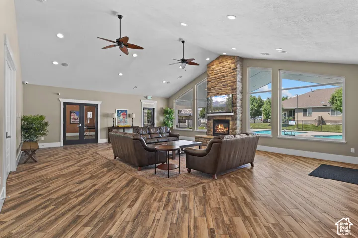 Vaulted ceiling, stone-surround fireplace, wood-finish flooring, dual ceiling fans, and expansive windows