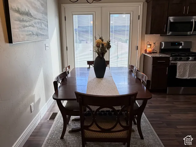 Dining space featuring wood-finish flooring, dark-toned cabinetry, stainless steel appliances, a classic multi-arm chandelier, and glass-paneled double doors