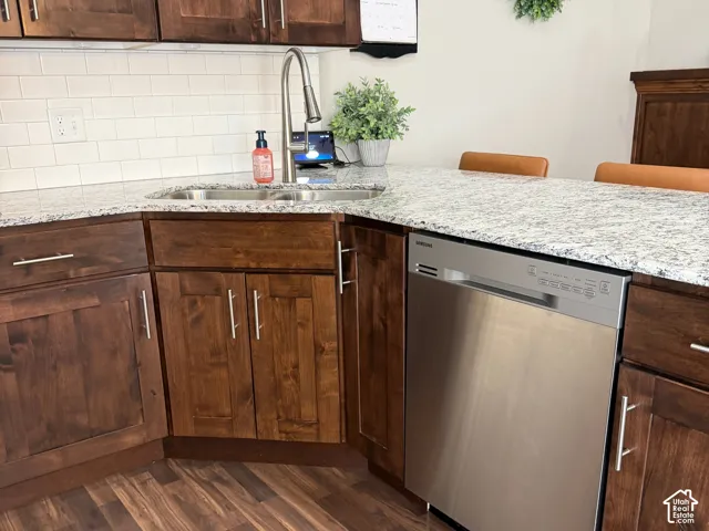 Kitchen featuring stained wood cabinetry, light-toned stone-finish countertops, stainless steel dishwasher, undermount sink with a high-arch pull-down faucet, and white subway tile backsplash