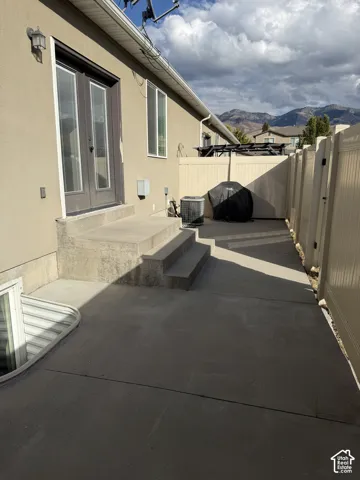 Concrete patio featuring double glass doors, a concrete staircase, mountain backdrop, and enclosed vinyl fencing