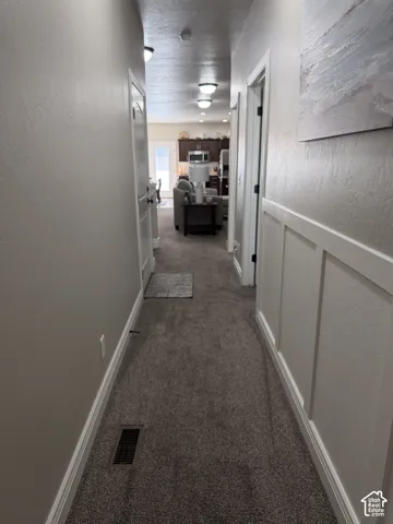 Hallway featuring textured walls, white board-and-batten wainscoting, carpeted flooring, and recessed ceiling lighting
