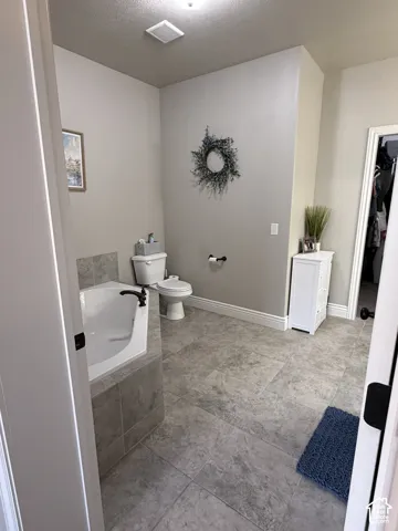 Primary suite bathroom offers a corner soaking tub with tile surround, matte black faucet, and stone-finish floor tile