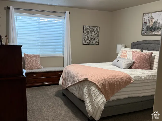 Neutral-toned bedroom featuring wall-to-wall carpeting, a large window with horizontal blinds, and a built-in wooden storage bench beneath the window