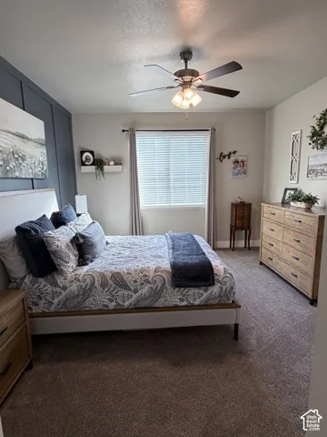 Bedroom featuring a charcoal-painted accent wall with vertical board-and-batten detailing, neutral wall-to-wall carpeting, and a central ceiling fan with integrated lighting