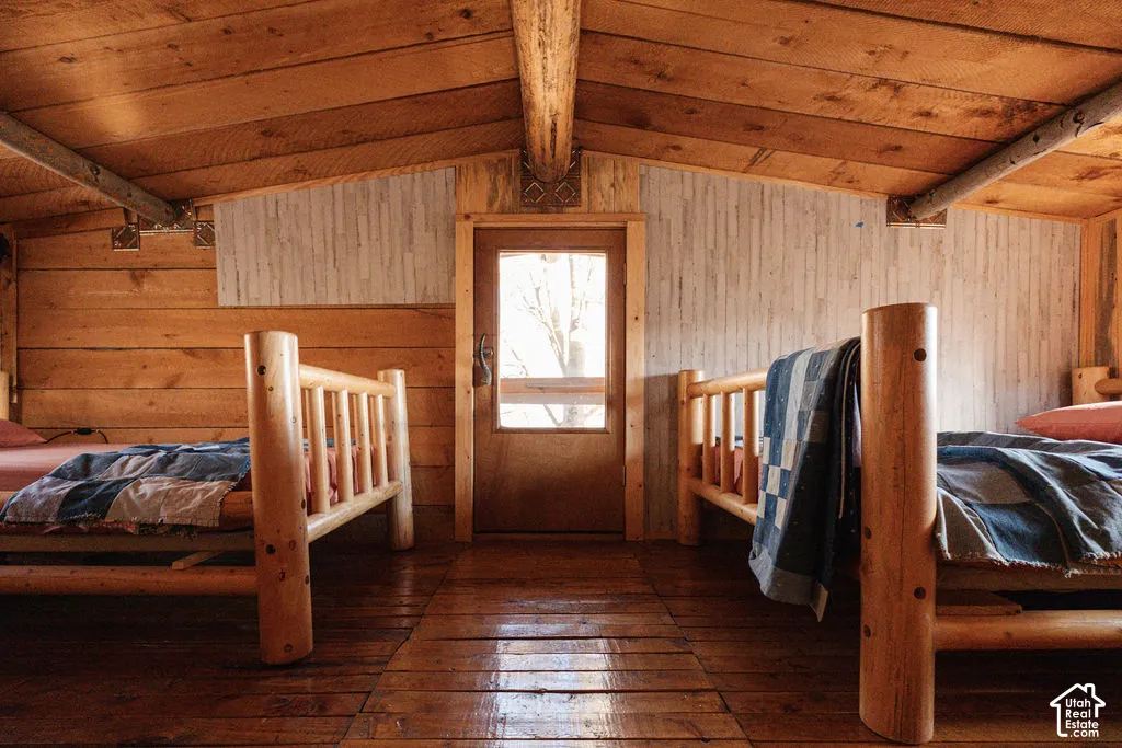 Rustic interior featuring exposed wood-plank walls and ceiling, heavy timber structural beams, wood-finish flooring, and a glass-paneled entry door