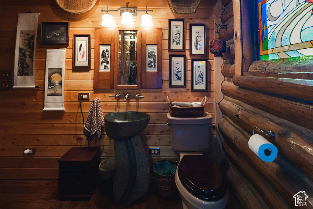 Log wall construction featuring a natural stone pedestal sink, wall-mounted metal faucet, stained wood cabinetry, and a custom stained-glass window