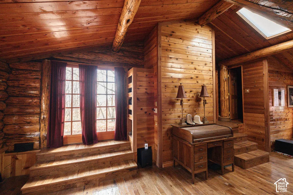 Interior space featuring exposed log walls, vaulted wood-plank ceilings, wood-finish flooring, multi-pane glass doors, and a skylight