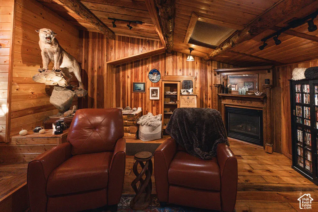 Interior featuring tongue-and-groove wood wall paneling, exposed log ceiling beams, natural wood flooring, a fireplace with a carved wooden mantel, and a built-in cabinetry unit