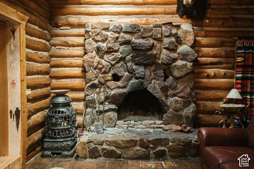 Full-log wall construction featuring a floor-to-ceiling dry-stack stone fireplace with an arched hearth, accompanied by an ornate cast-iron freestanding stove and hardwood flooring