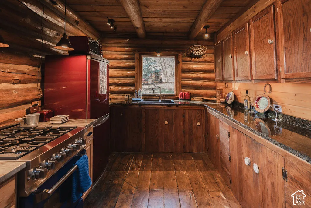 Kitchen featuring exposed log walls, solid wood cabinetry, dark stone countertops, wood flooring, and exposed ceiling beams