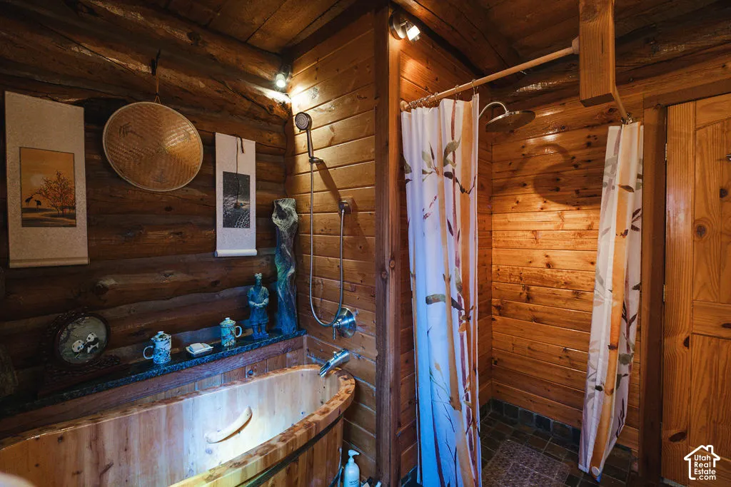 Bathroom featuring exposed log walls, a wood-finish soaking tub, a built-in stone-top ledge, a wall-mounted shower fixture, and a solid wood door