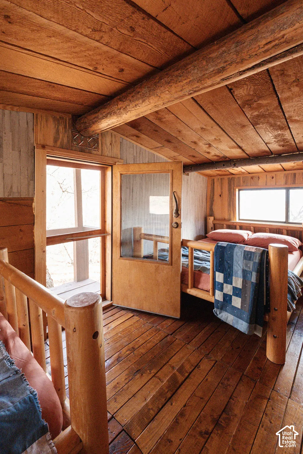 Interior space featuring exposed log structural beams, wood-plank ceiling, wood-finish flooring, and a glass-panel door