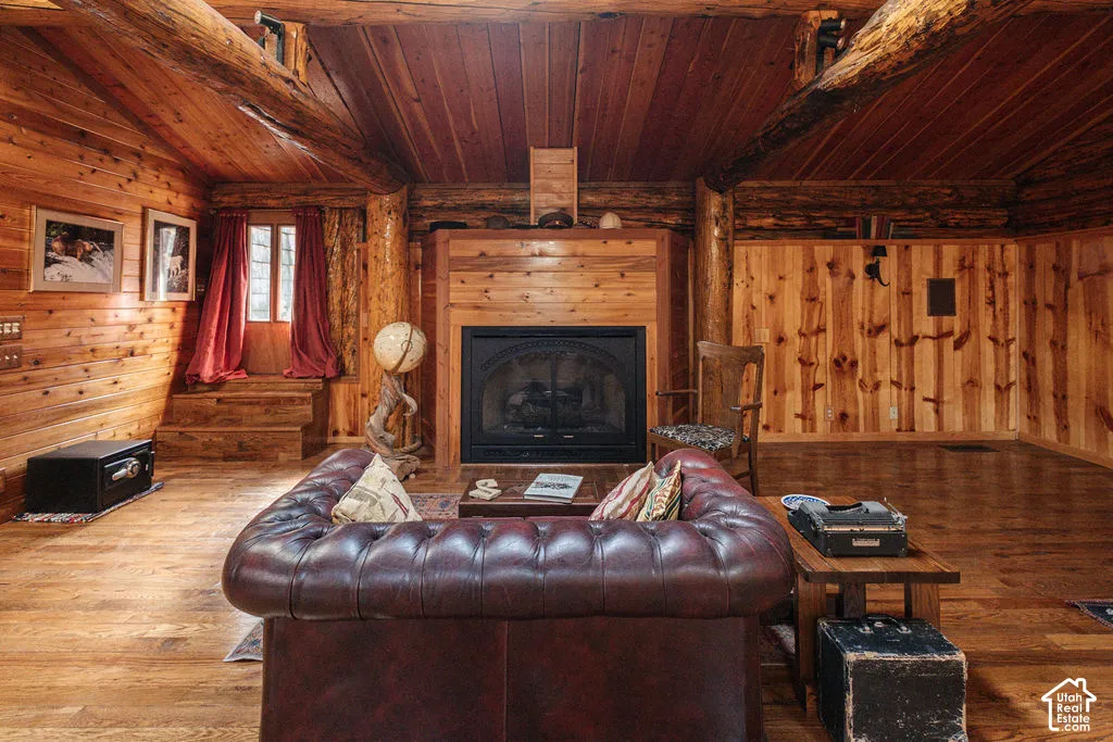 Log-style interior featuring exposed timber beams, wood-plank walls, wood-finish flooring, and a floor-to-ceiling wood-encased fireplace