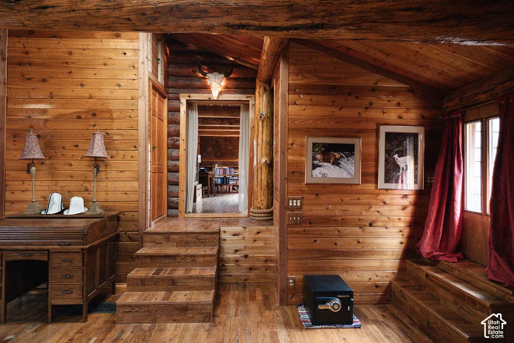 Interior featuring exposed log timber walls, horizontal wood-plank paneling, vaulted beamed ceilings, and custom wood staircases