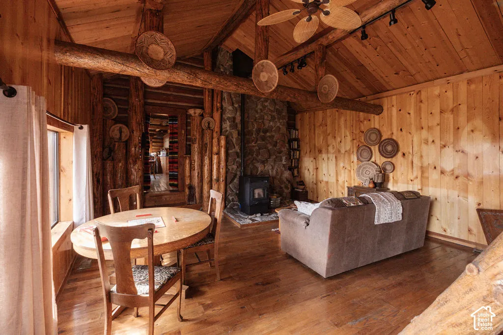 Vaulted ceiling with exposed log beams, natural wood wall paneling, stone hearth, wood-burning stove, and wood-finish flooring