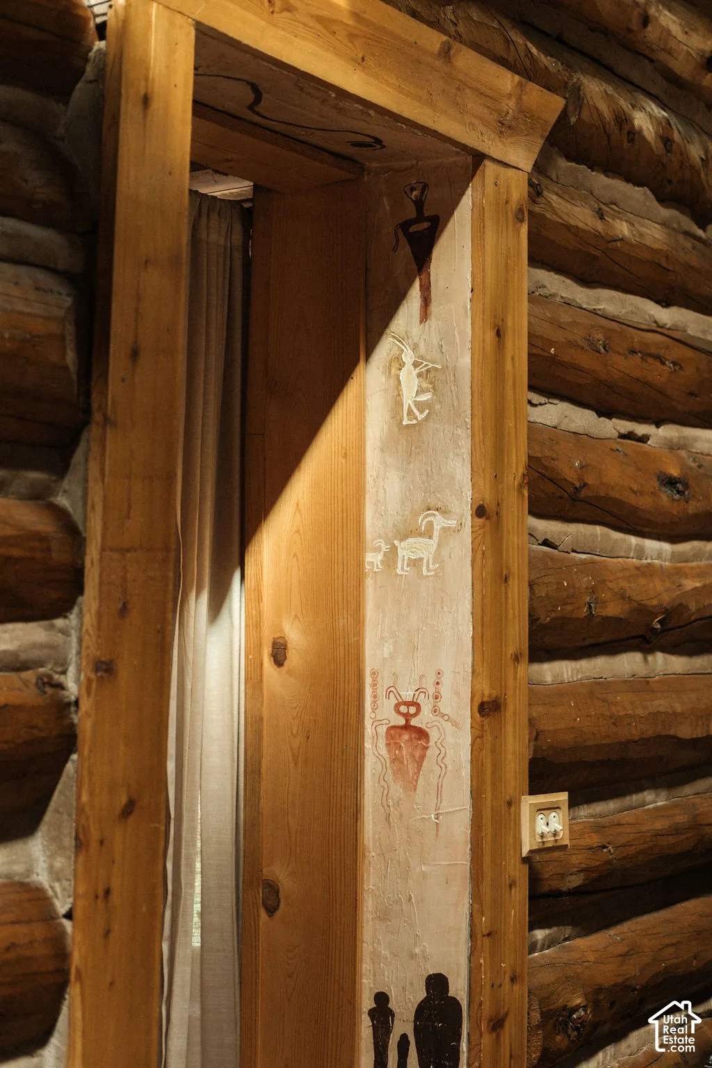 Hand-hewn log walls featuring traditional chinking, complemented by a custom wood door casing and decorative hand-painted masonry accents