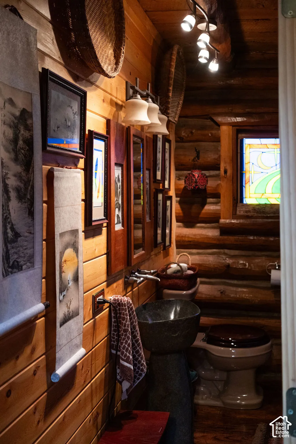 Interior space featuring exposed log walls, a pedestal stone-composite sink, stained glass window, and multi-directional track lighting