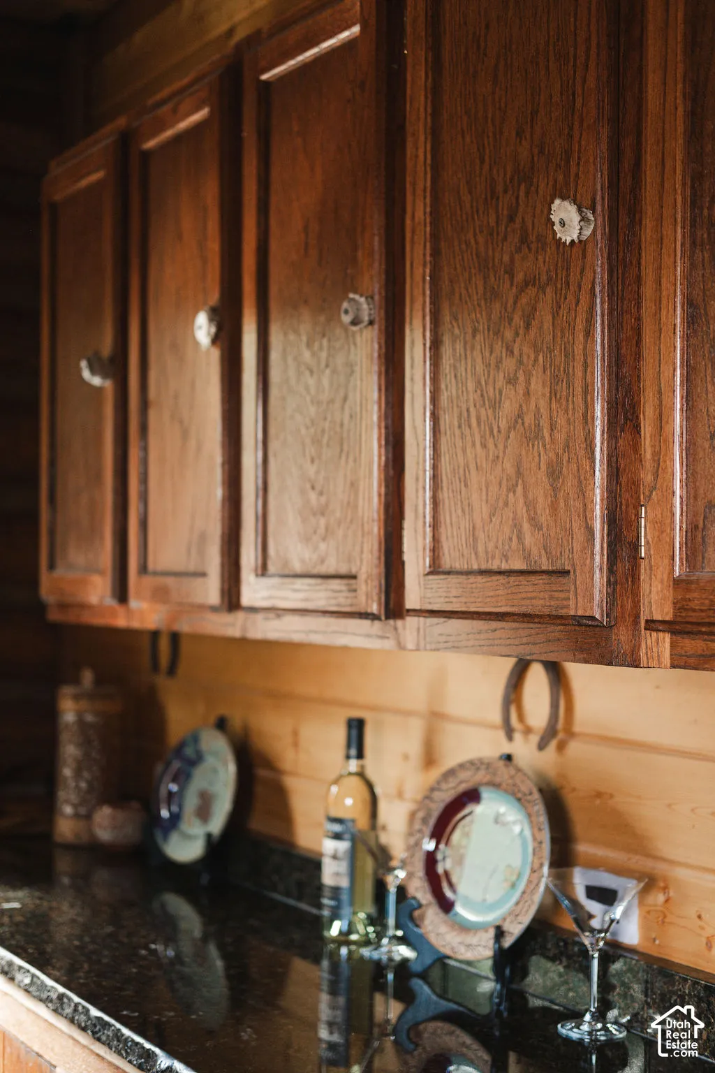 Rich-toned wood cabinetry with vertical grain detailing and custom antler-style hardware, accompanied by dark stone-surface countertops and horizontal wood-plank wall paneling