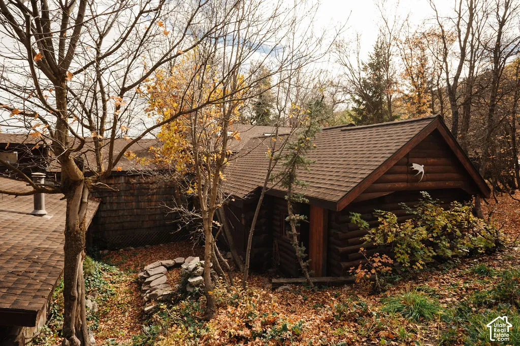 Log exterior siding featuring a gabled shingle roof, stone-accented hardscaping, and mature deciduous trees