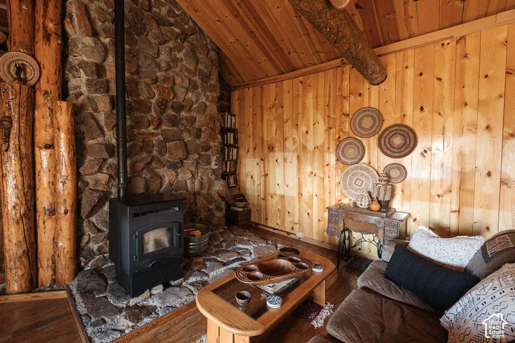 Floor-to-ceiling natural stone hearth, cast-iron wood stove, tongue-and-groove wood wall paneling, exposed log structural beam, and vaulted wood-paneled ceiling
