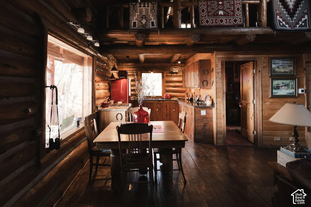 Log interior featuring horizontal log walls, exposed timber ceiling beams, wide-plank wood flooring, and a mezzanine level with a wooden railing