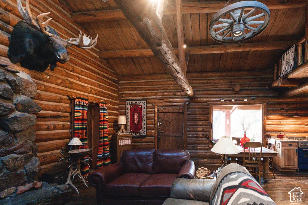 Exposed log walls, vaulted wood-beam ceiling, stone masonry fireplace, and custom wagon wheel light fixture