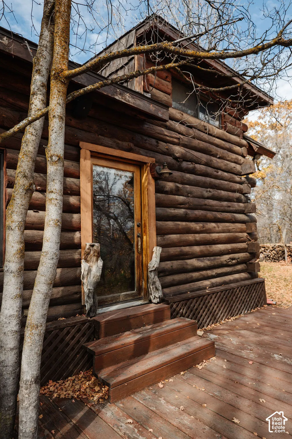 Exterior log construction featuring a natural wood deck, lattice skirting, and a glass-paneled entry door with wood casing