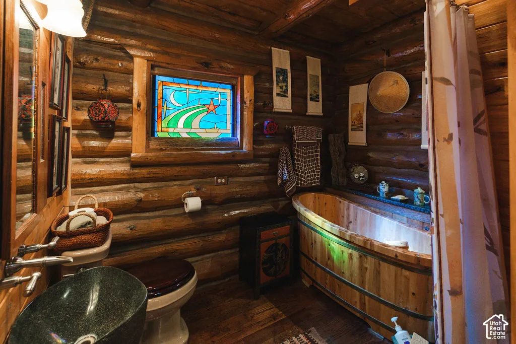 Bathroom featuring exposed log walls, a custom wood-barrel soaking tub, a decorative stained-glass window, and a dark stone vessel sink