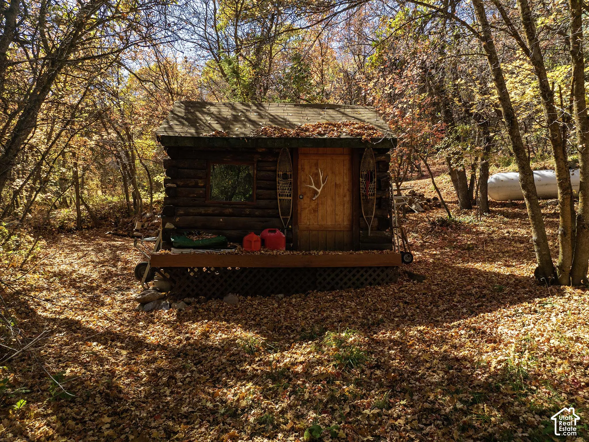 Log cabin structure featuring horizontal log exterior walls, a gabled roof, a wood-plank entry door, and an attached elevated wooden deck with lattice skirting