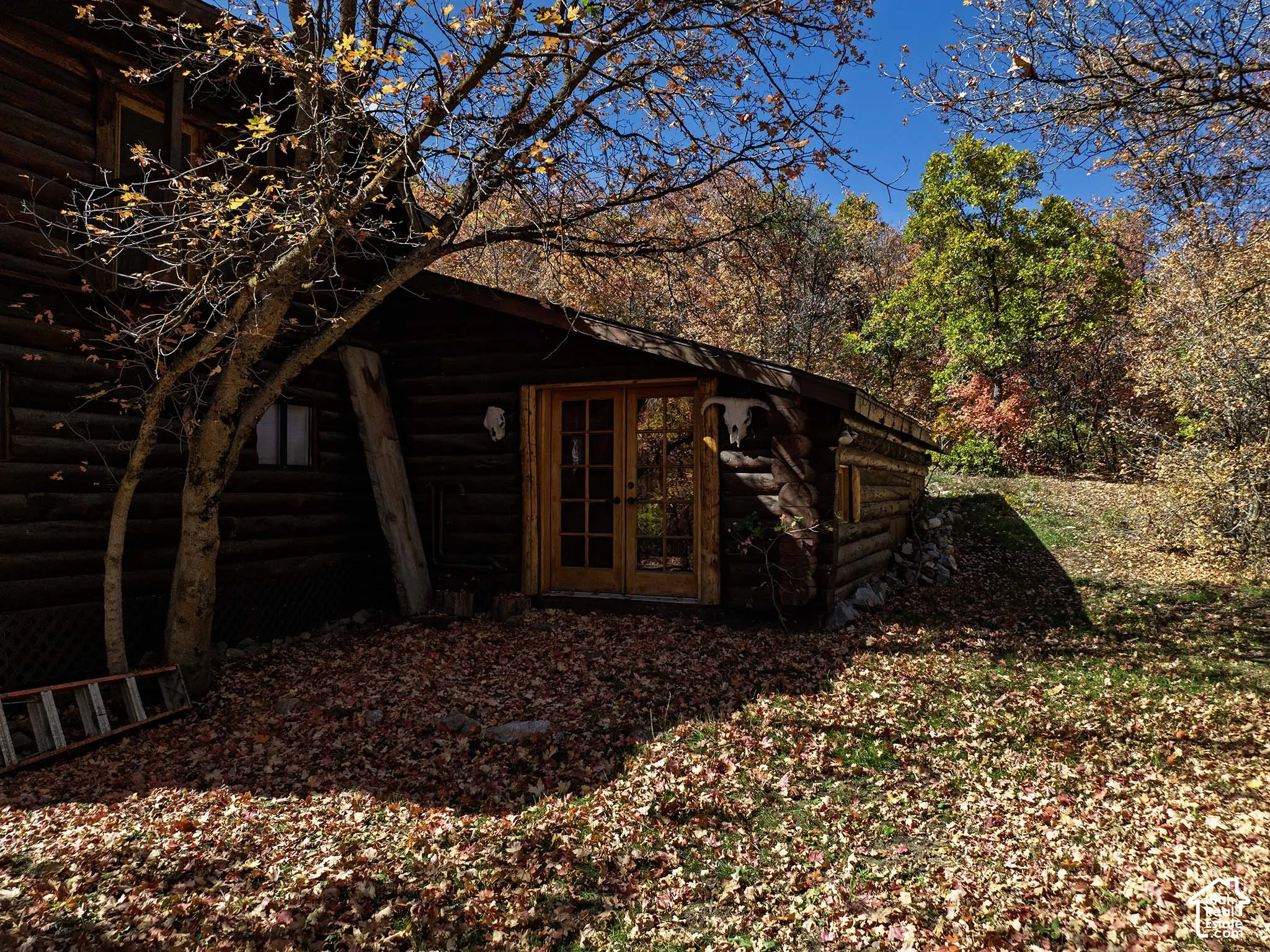 Log exterior residence featuring stacked timber construction, natural stone retaining wall, and wood-framed glass paneled doors