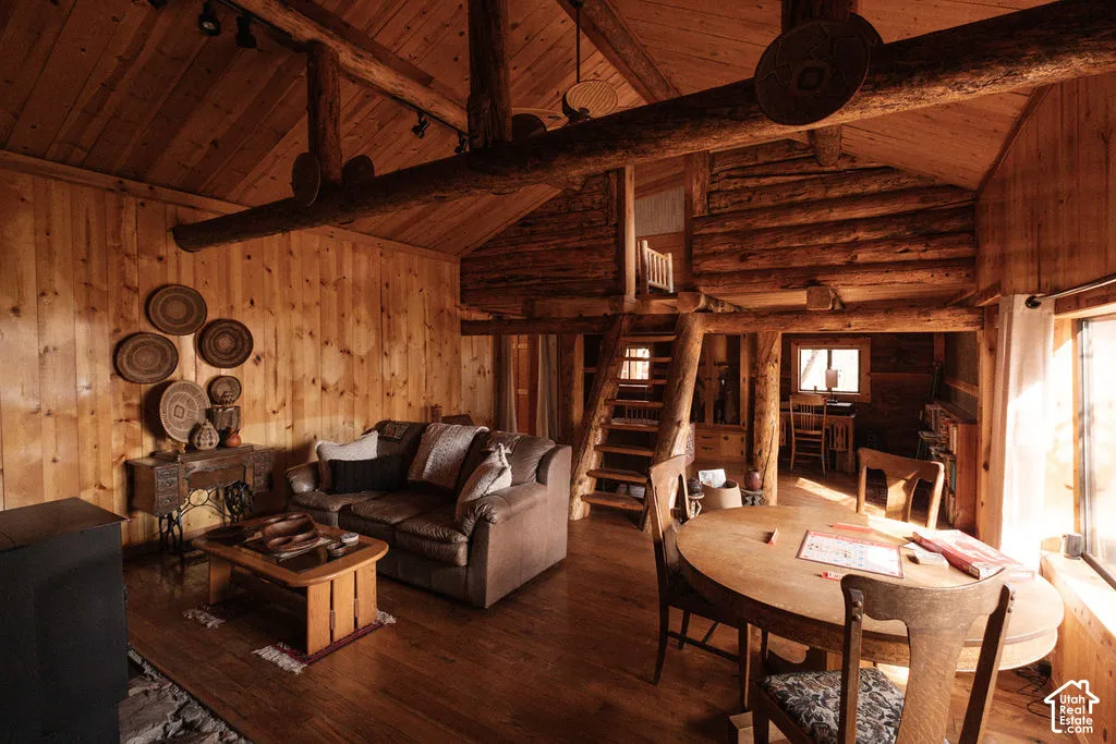 Interior space featuring exposed log walls, timber beam vaulted ceilings, wood-finish flooring, a built-in wooden staircase, and a wood-burning stove on a stone hearth