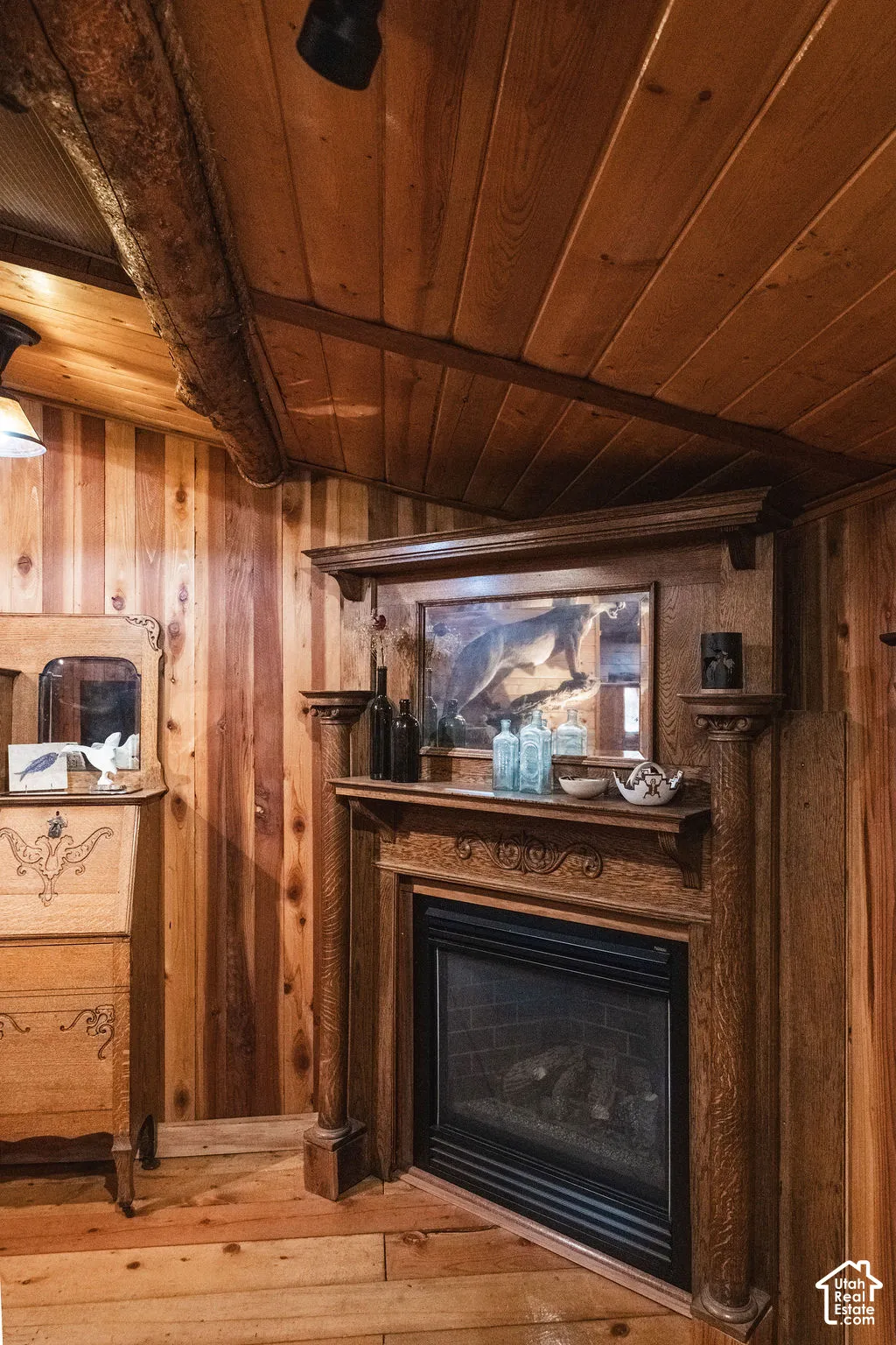 Wood-paneled interior featuring a fireplace with an ornate wooden mantel and decorative columns, vaulted ceiling with exposed log beam, and wood-finish flooring