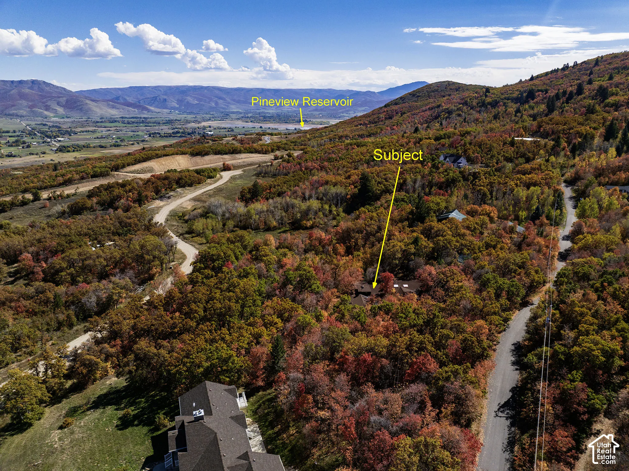 Aerial perspective showcasing a secluded property site situated within a dense landscape of mature deciduous trees and mountainous terrain, with distant mountain range scenery and proximity to Pineview Reservoir