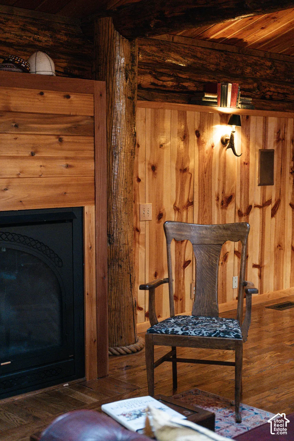 Rustic interior featuring vertical wood-plank wall paneling, a full-log structural support column, and a built-in fireplace with a black metal surround