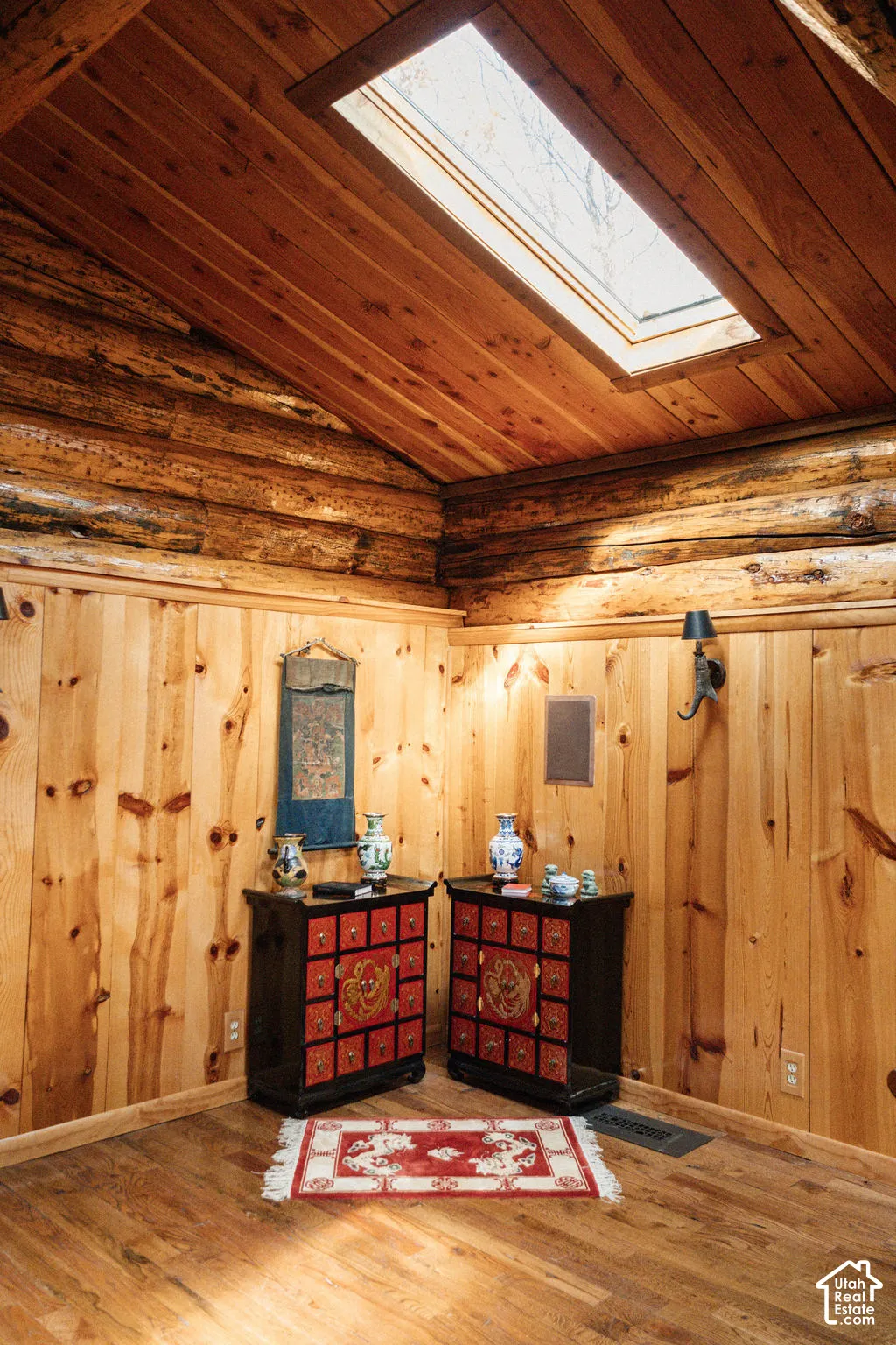 Log-style interior walls, natural wood-paneled walls, vaulted ceiling with wood-plank finish, skylight, and wall-mounted light fixture