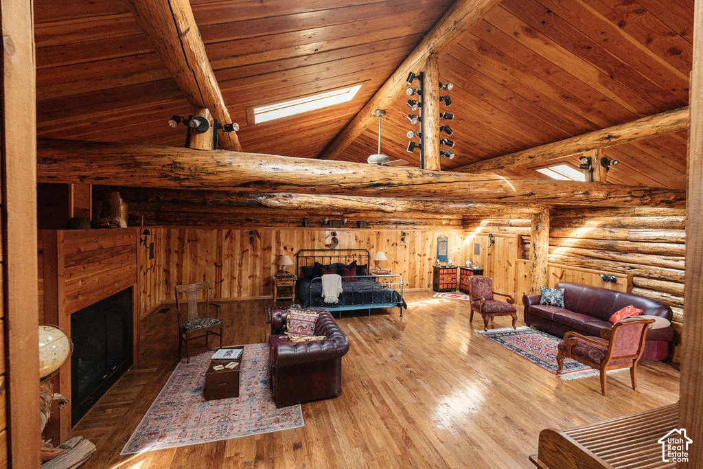 Vaulted ceiling with exposed log beams, horizontal log walls, wood-finish flooring, built-in fireplace, and integrated skylights