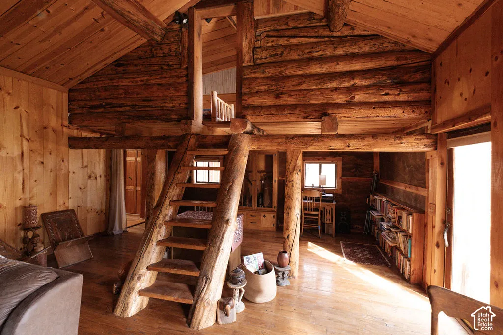 Rustic log construction with exposed timber ceiling beams, natural wood-finish walls, built-in wooden shelving, and a prominent log-frame staircase